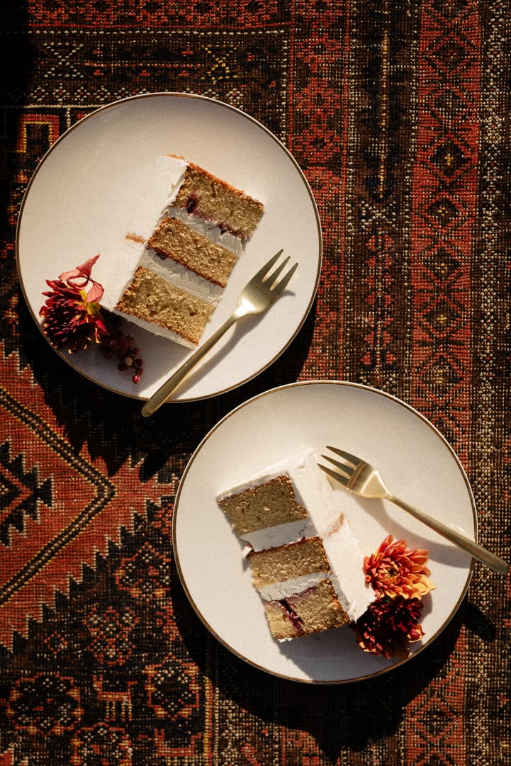 Two plated cake slices with gold forks and florals on a patterned rug in warm light