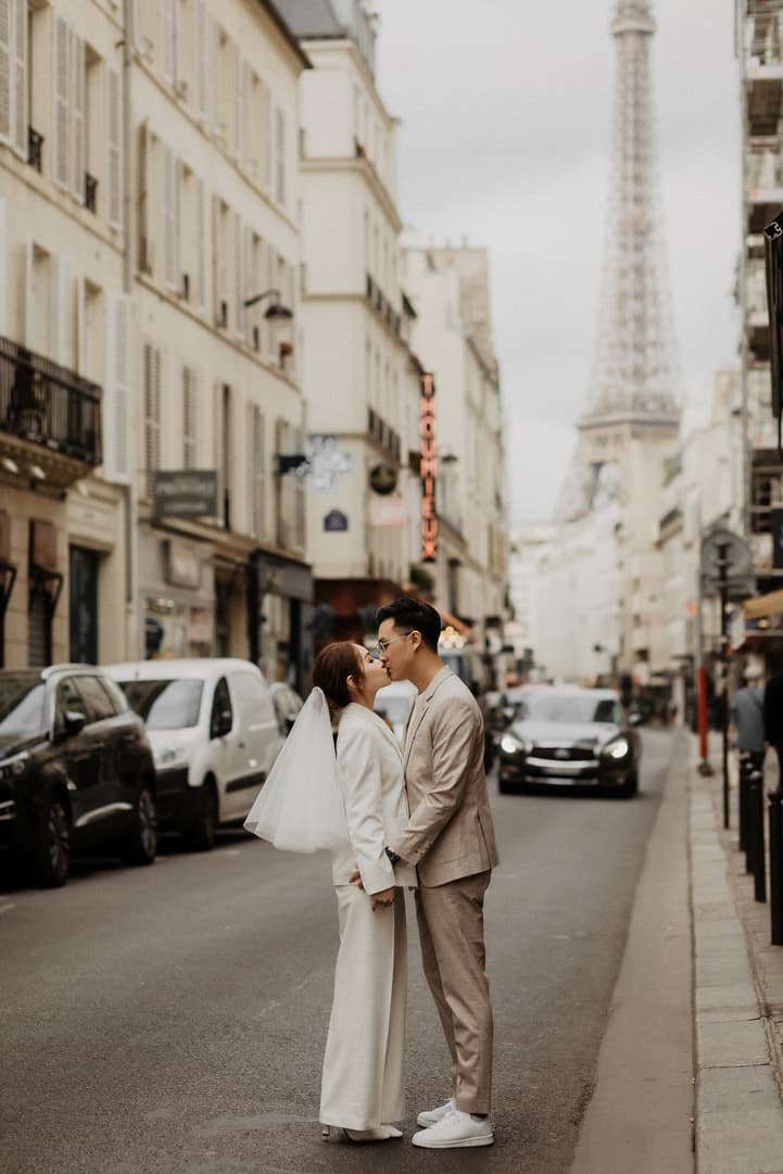 Bride and groom kiss on a Paris street with the Eiffel Tower rising in the mist behind them
