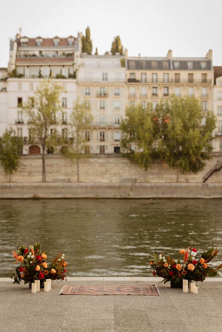Floral arrangements and candles line a riverside terrace beside the Seine at golden hour