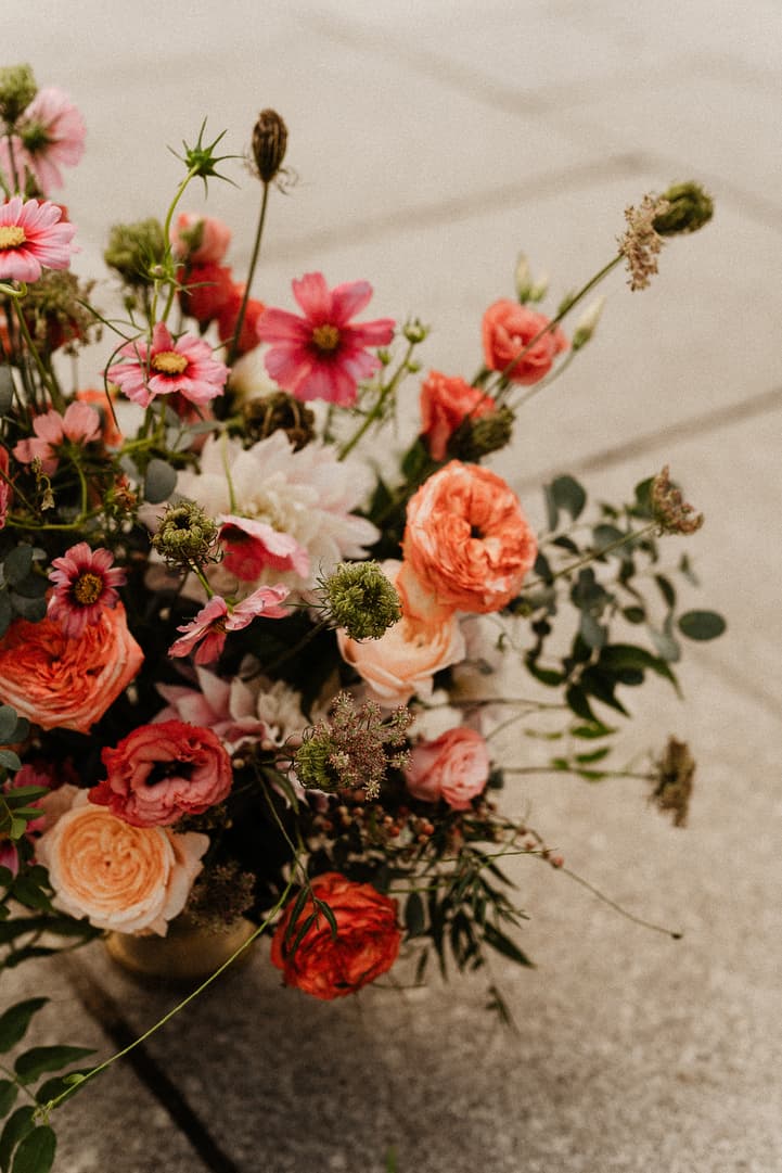 Loose pink and coral wedding flowers spill from a vase onto a stone floor