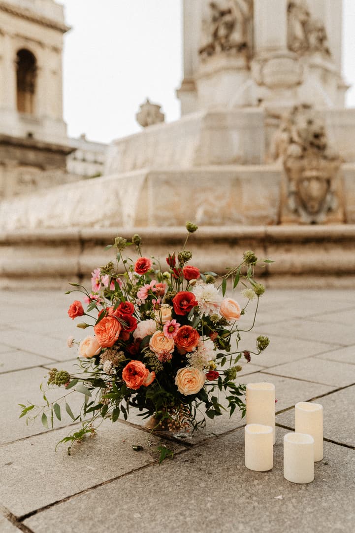 A floral arrangement and four candles rest on a Paris plaza before a stone fountain