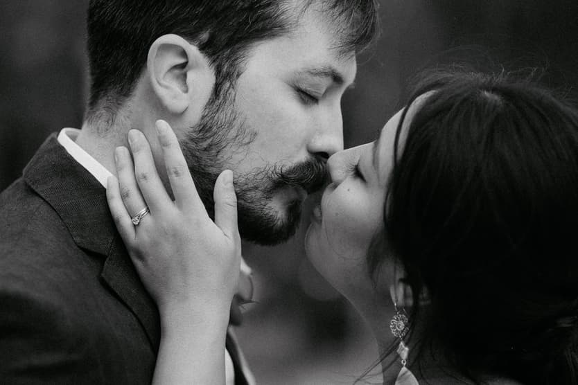 Bride and groom kiss in a black-and-white close-up, her hand on his cheek