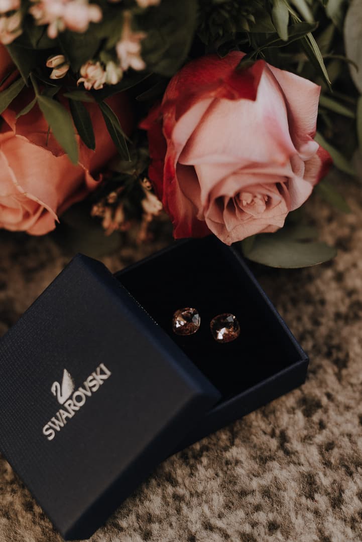 Pink roses and a Swarovski earring box rest on a carpet in soft, warm light