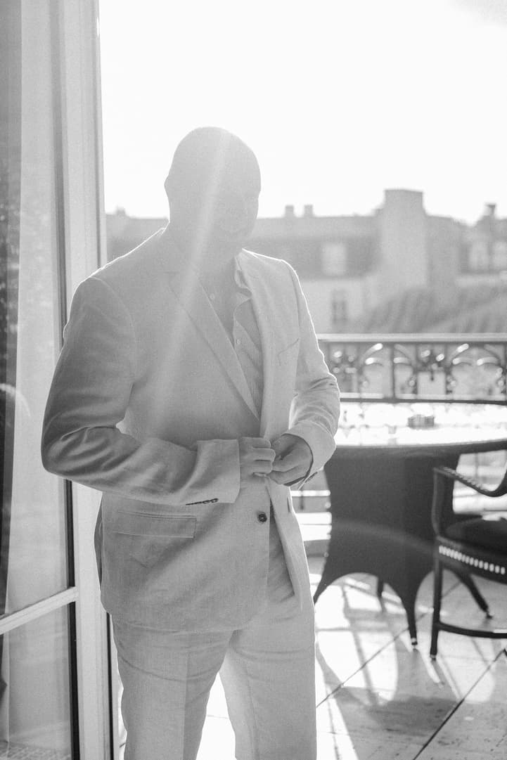 Groom buttoning his jacket on a sunlit Paris balcony with wrought-iron railings