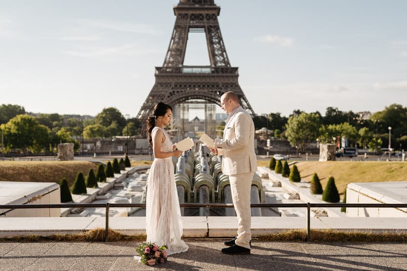 Bride and groom exchange vows before the Eiffel Tower in warm light, with a bouquet at her feet