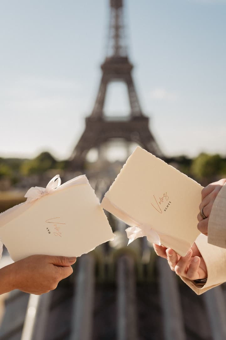 A couple holds vow books before the Eiffel Tower in warm golden light