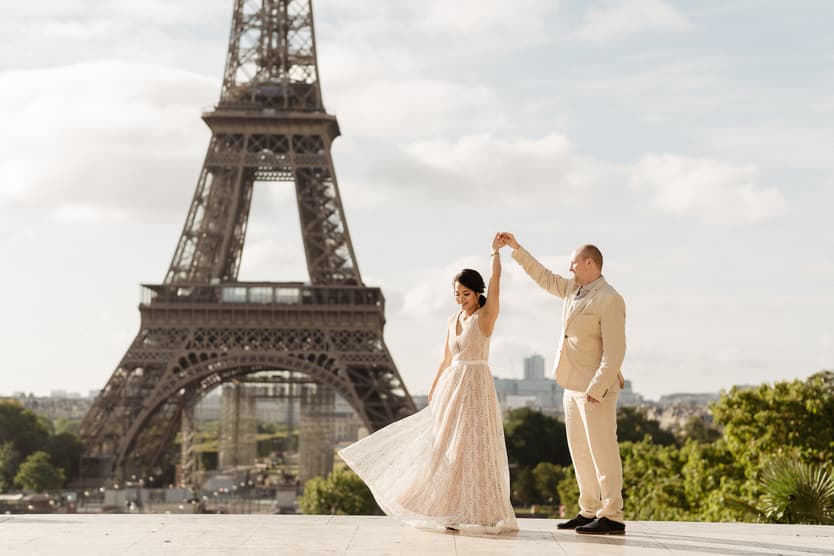 Bride and groom hold hands and twirl before the Eiffel Tower in soft daylight