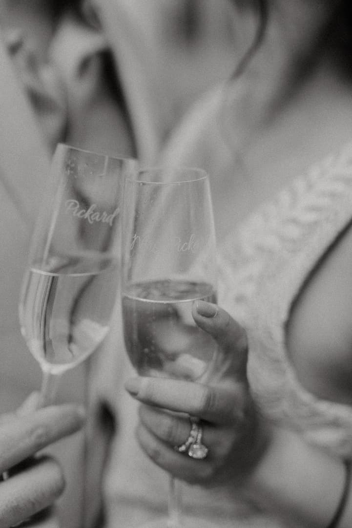 Bride and groom raise champagne flutes in a soft black-and-white closeup, her ring catching the light