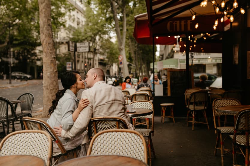 A couple kisses at a Paris street café under warm string lights and trees