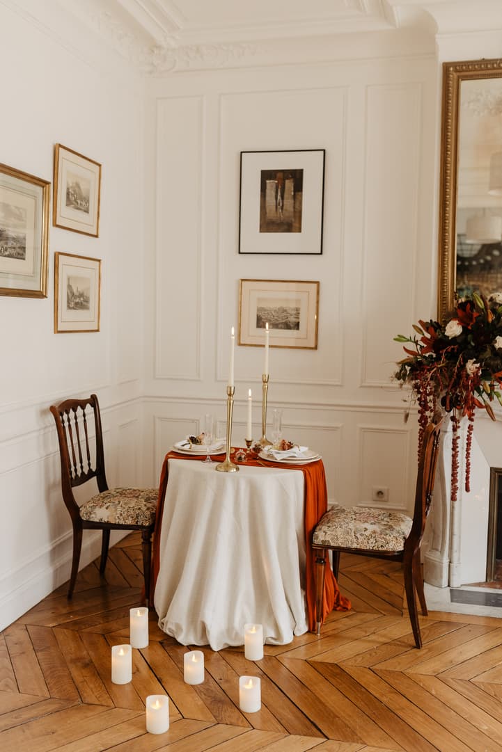 Romantic candlelit table for two in a Paris hotel room with orange draping and floral decor