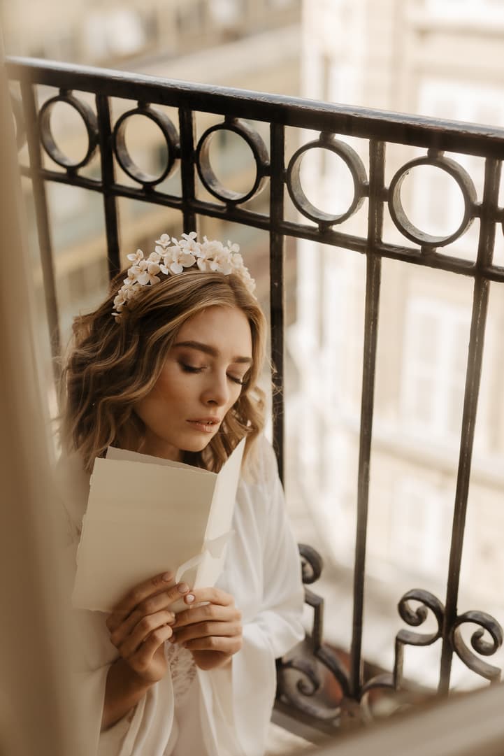 Bride in a floral headpiece reads letters on a Paris balcony in soft morning light