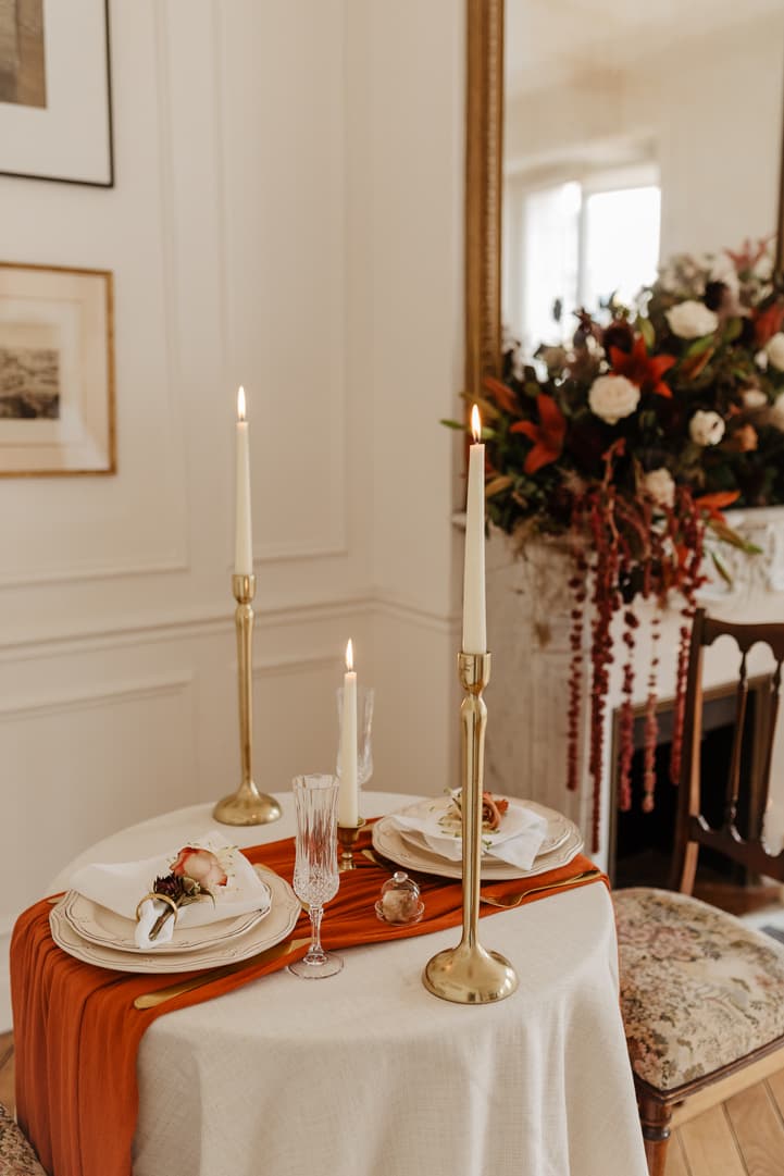 Candlelit elopement table in a Paris room with gold candlesticks, an orange runner, and a floral arrangement