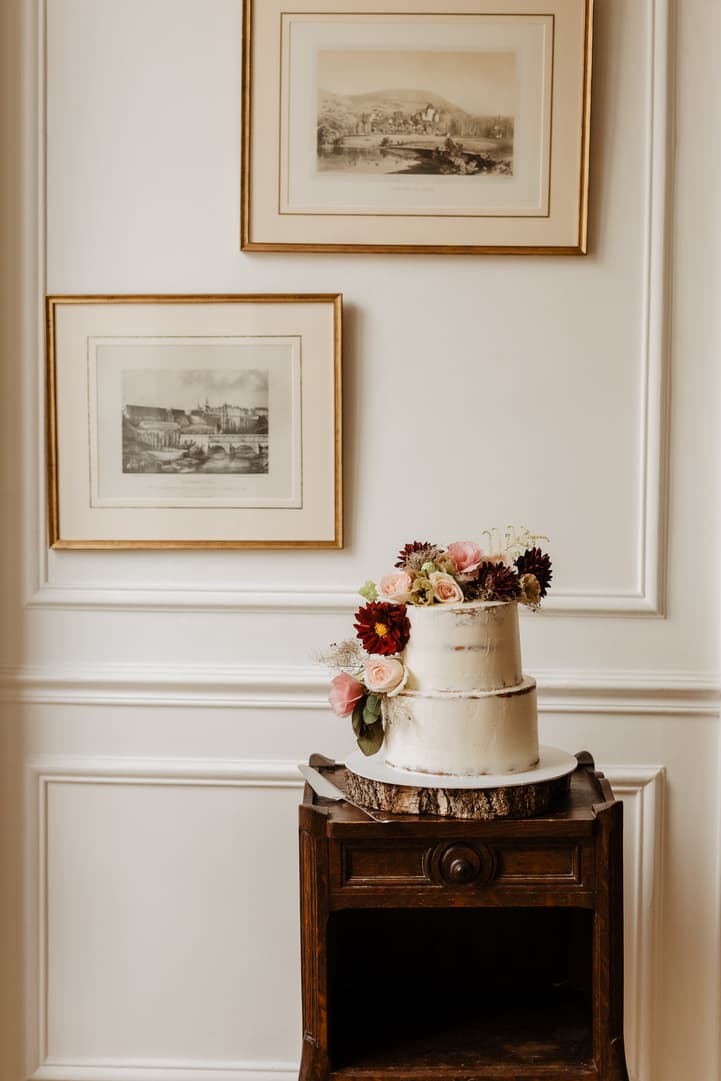 A floral two-tier wedding cake stands on a wooden table in a softly lit room