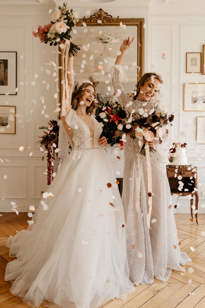 Bride and partner celebrate amid confetti in a bright Paris salon, bouquets raised