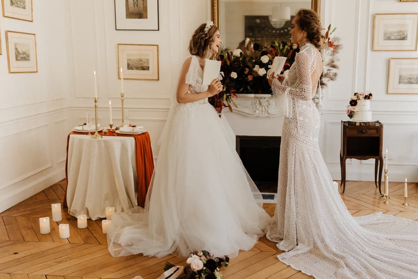 Bride and officiant talk in a candlelit Paris salon with bouquets, framed art, and a mantel mirror