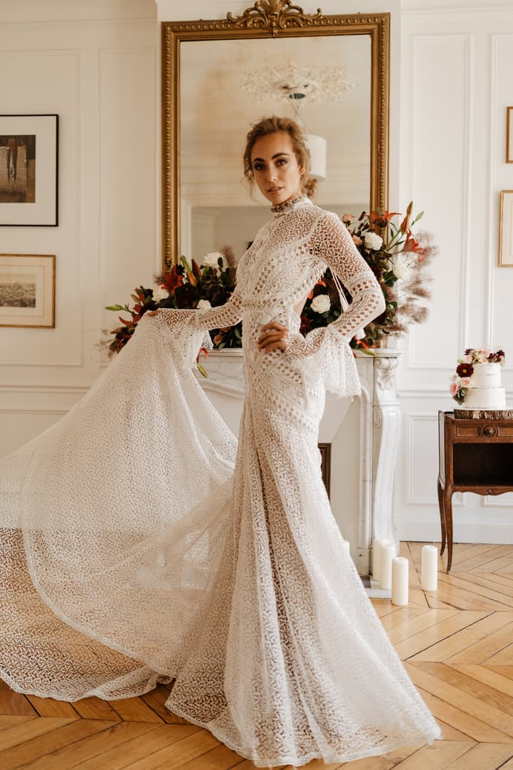 Bride in a lace gown poses in a Paris salon with flowers, candles and a gold-framed mirror