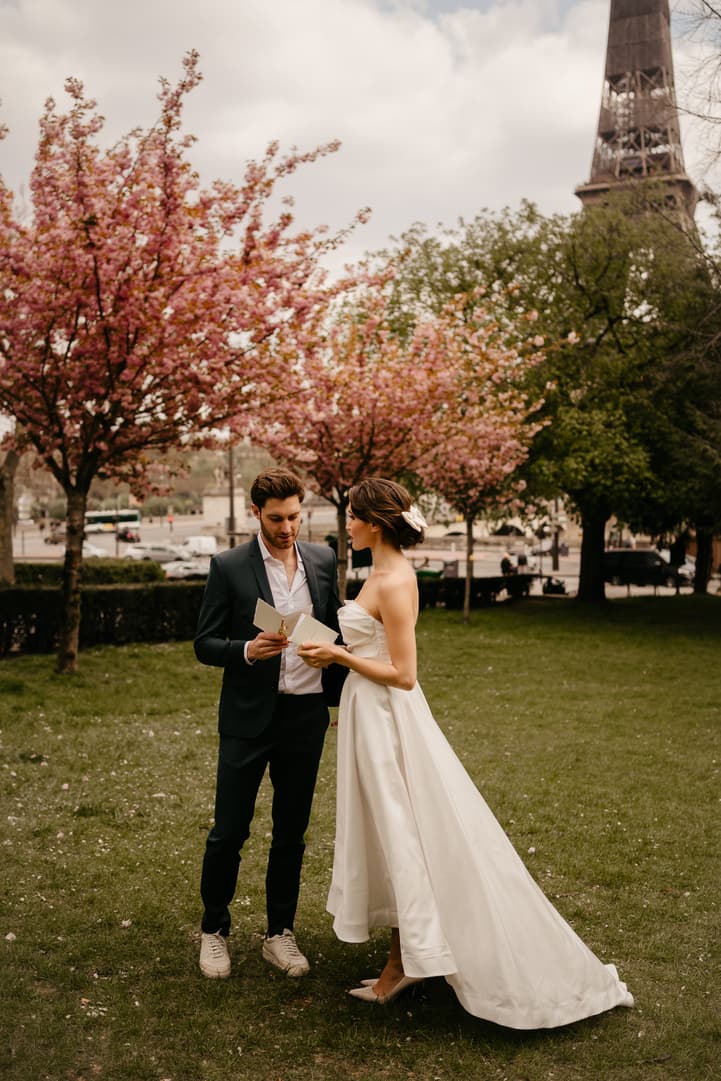 Bride and groom read vows beside blooming trees with the Eiffel Tower rising behind them