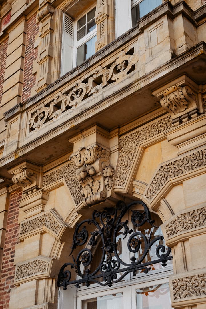 Ornate stone townhouse facade on a Paris street with black wrought-iron window grille