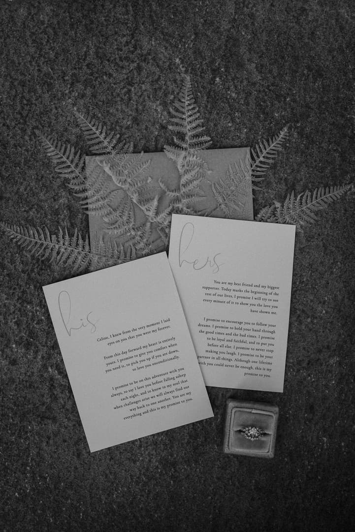 Handwritten wedding vows, fern fronds and a ring box arranged on dark velvet fabric