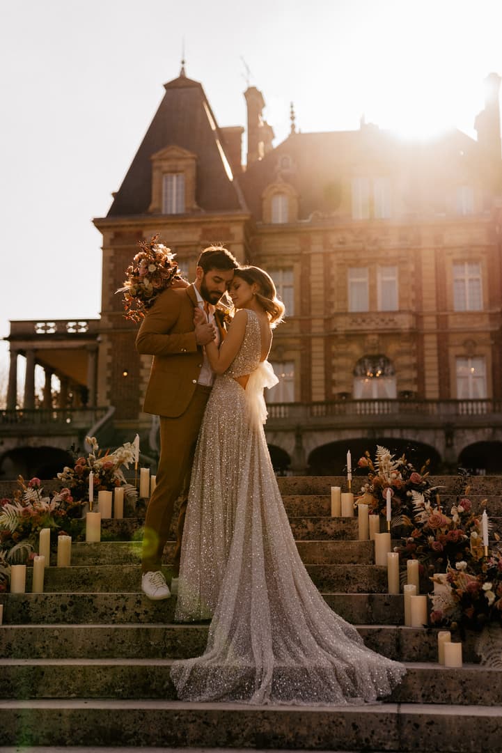 Bride and groom embrace on candlelit steps before a historic Paris mansion at sunset