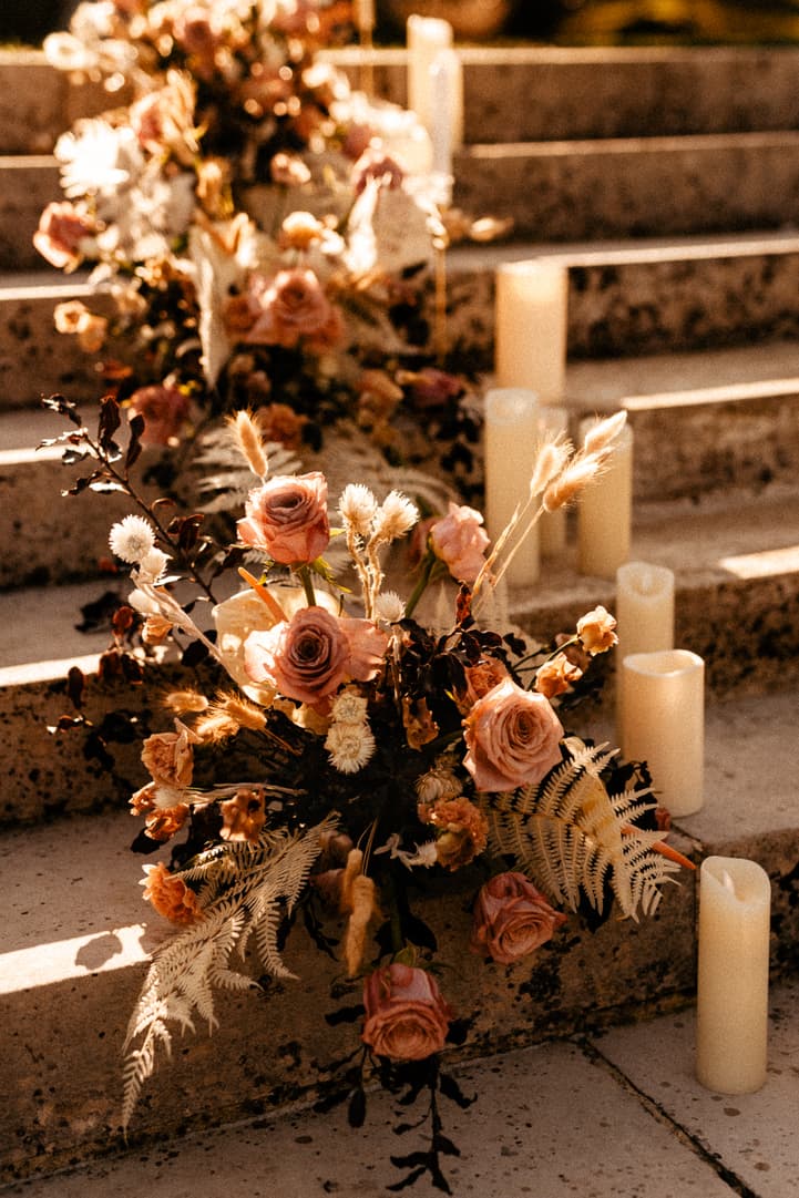 Floral arrangements and pillar candles line stone steps in warm golden light