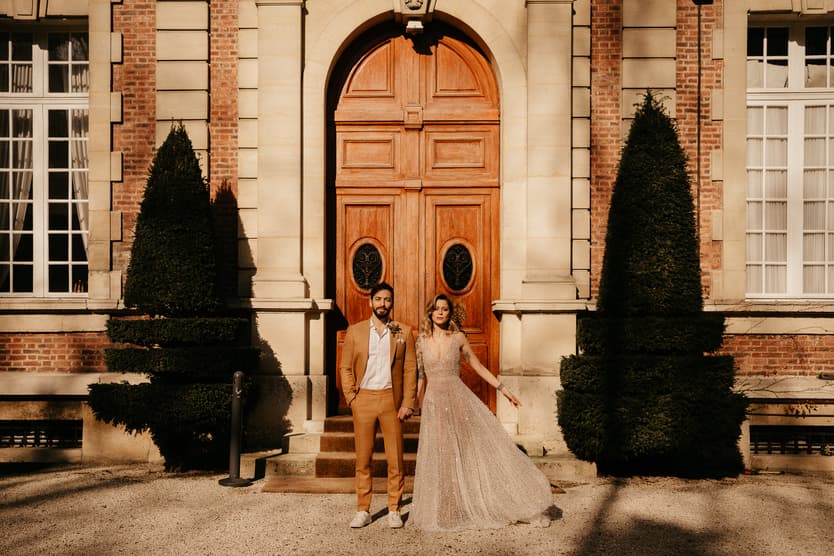 Bride and groom stand before a grand Paris doorway in warm afternoon light