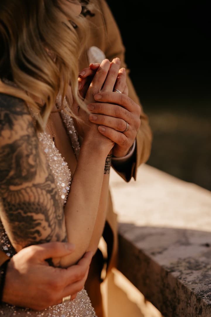Bride and groom clasp hands in warm sunlight beside a stone terrace on a Paris street