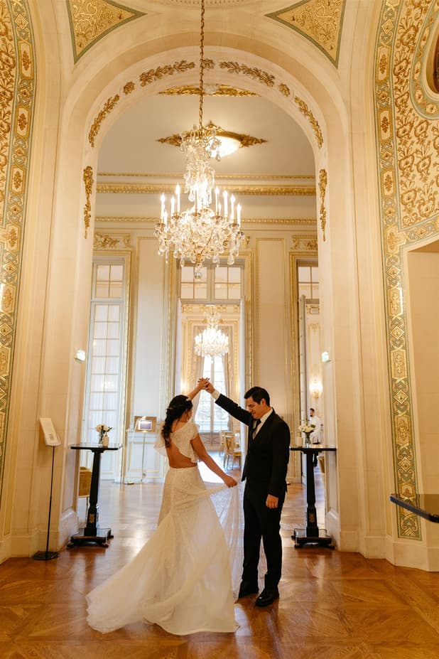 Bride and groom dance under a chandelier in an ornate Paris hall with gilded mirrors