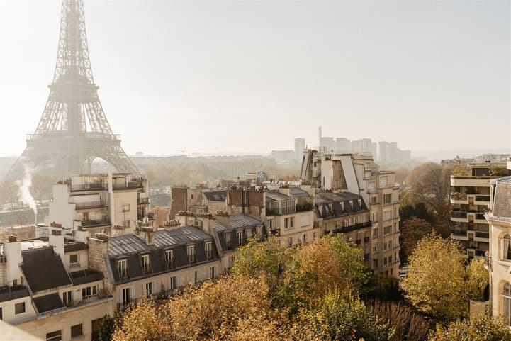 The Eiffel Tower rises above Paris rooftops and autumn trees in soft morning light