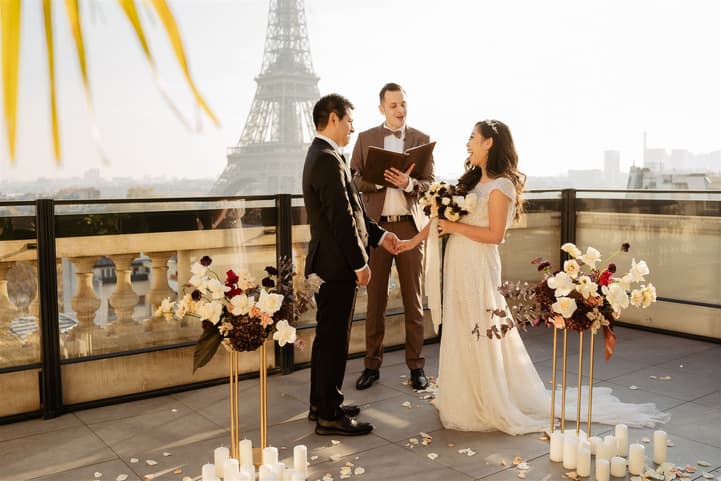Bride and groom exchange vows with an officiant on a terrace, with the Eiffel Tower glowing behind them