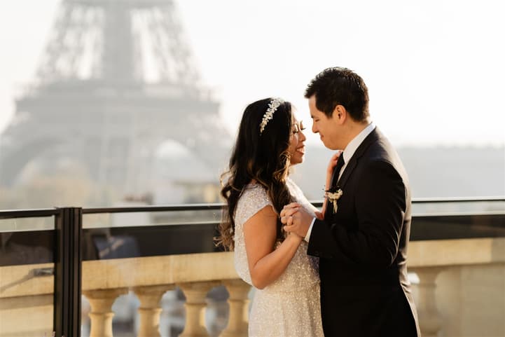 Bride and groom hold hands on a Paris terrace with the Eiffel Tower softly in the background