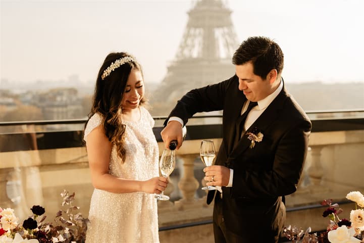 Bride and groom toast on a Paris terrace with the Eiffel Tower behind them in warm evening light