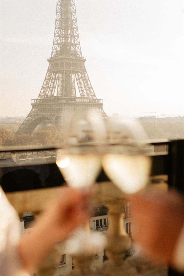 Champagne glasses toast before the Eiffel Tower, with warm light and blurred hands in foreground