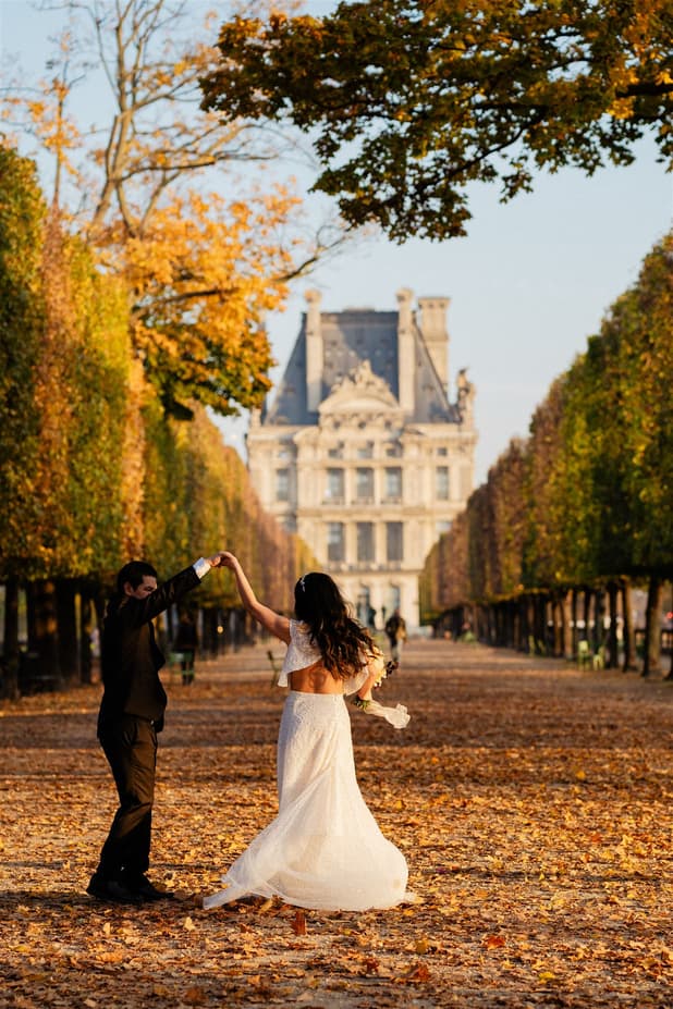 Bride and groom dance in golden autumn light on a garden path lined with trees
