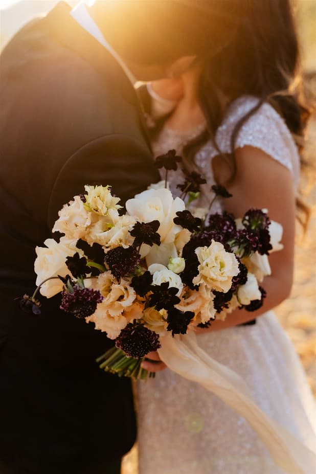 Bride and groom embrace on a Paris street, holding a bouquet in warm golden light