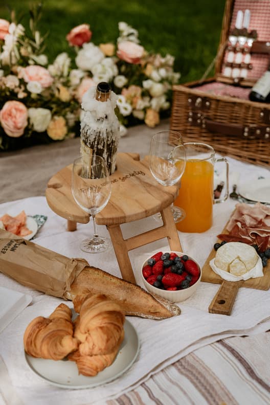 Wedding picnic spread on a blanket with pastries, fruit, cheese and orange juice beside flowers in a garden