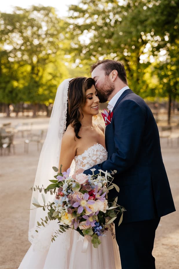 Bride and groom embrace in a garden at golden hour, with a colorful bouquet in the foreground