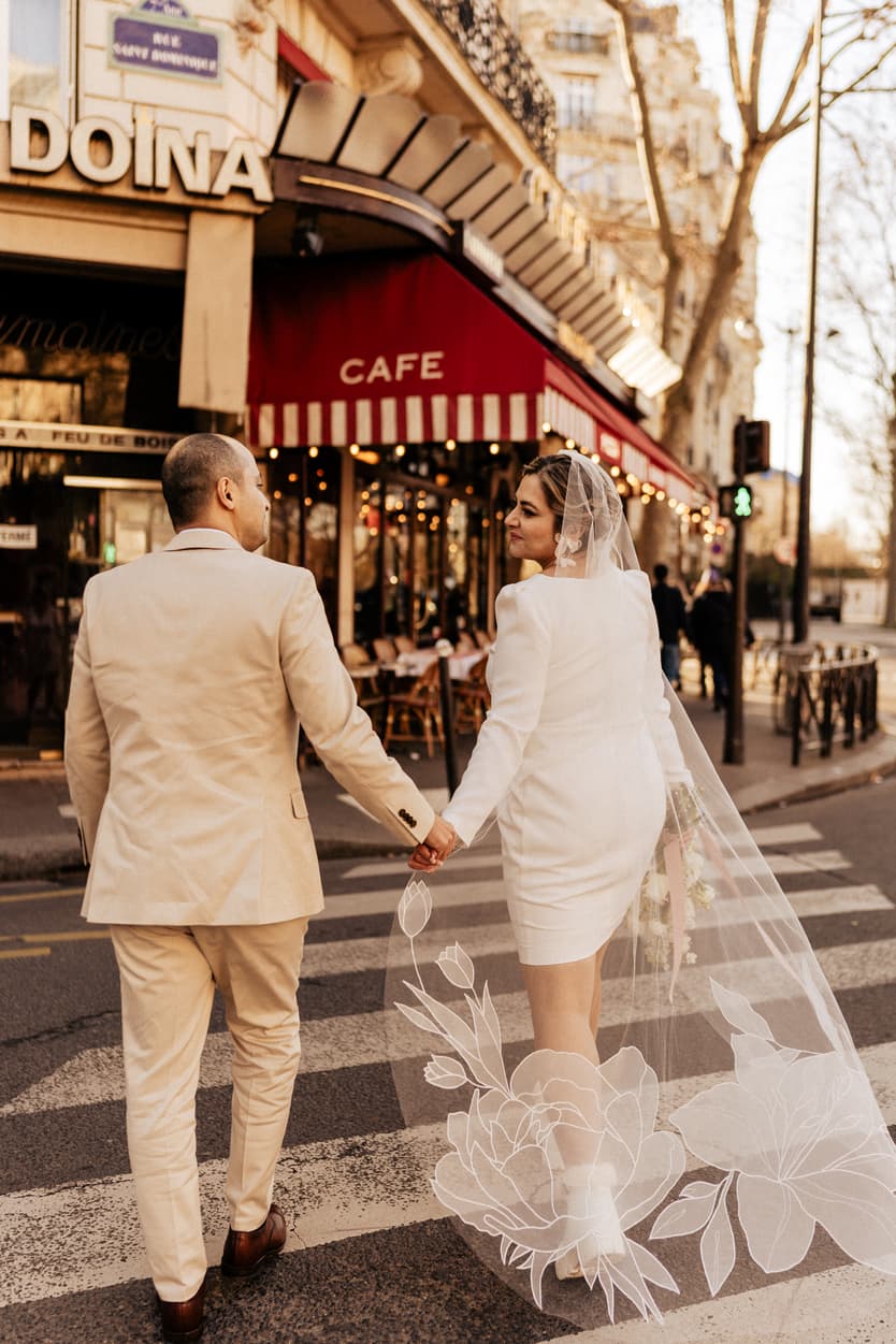 Bride and groom hold hands crossing a Paris street beside a café in warm evening light