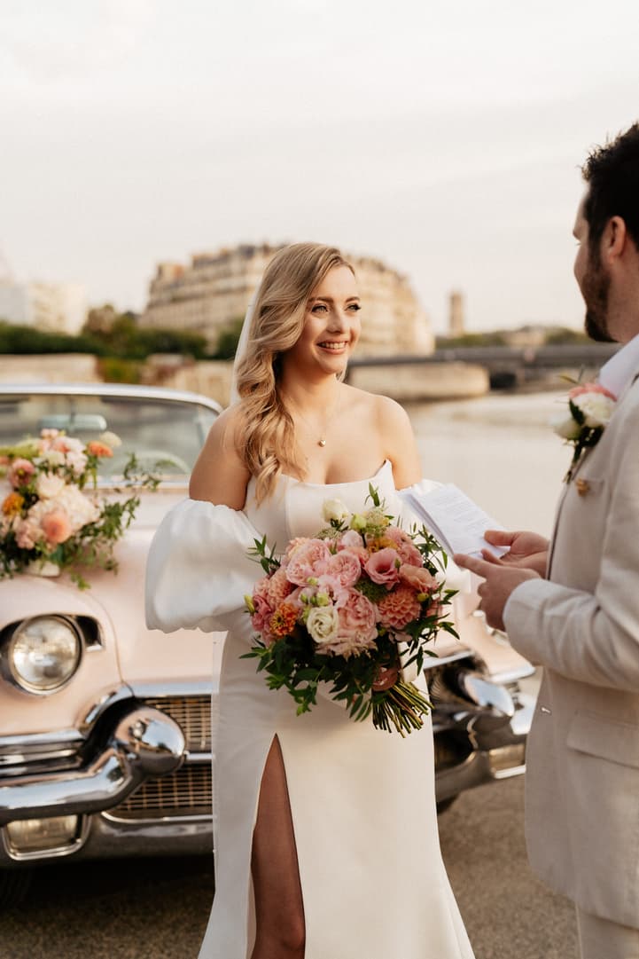 Bride and groom exchange vows beside a vintage car on a Paris street in warm evening light
