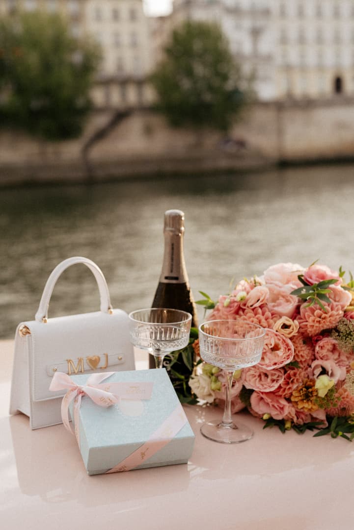 Wedding gifts, champagne flutes and pink flowers on a table beside the Seine in soft daylight