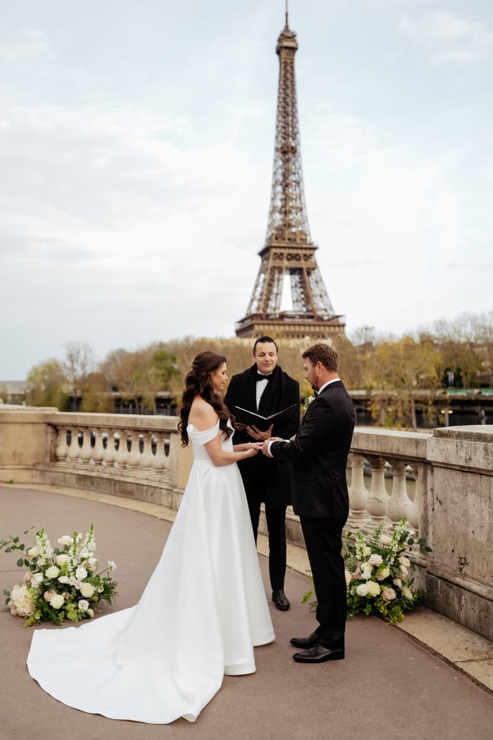 Bride and groom exchange vows with an officiant on a Paris terrace, the Eiffel Tower behind them