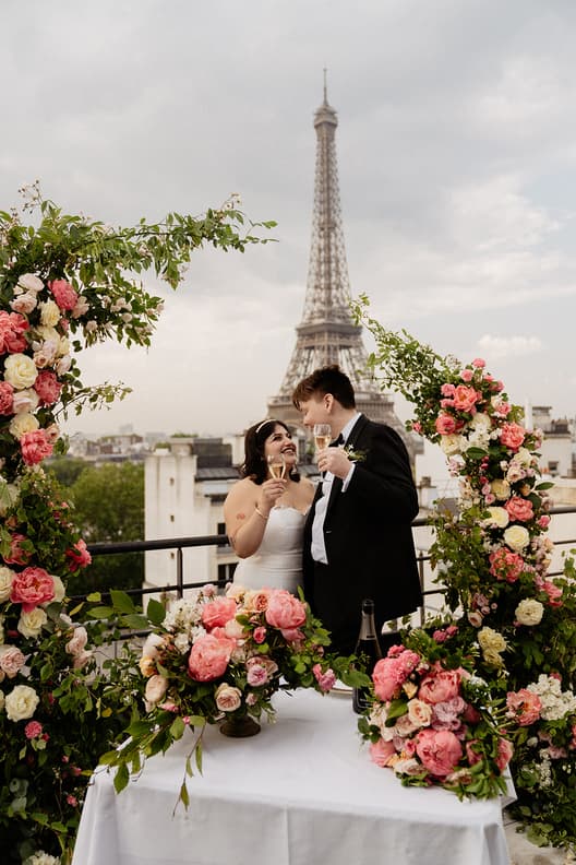 Bride and groom toast at a flower-covered rooftop table with the Eiffel Tower behind them