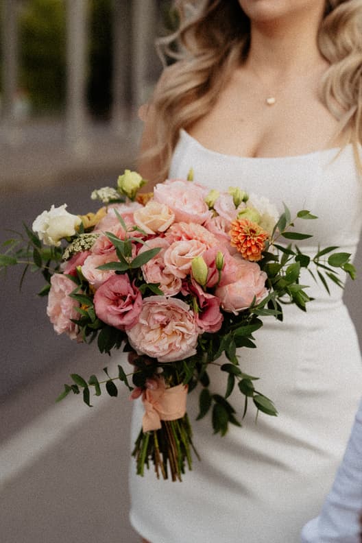 Bride in a white dress holds a pink and peach bouquet on a Paris street in soft light