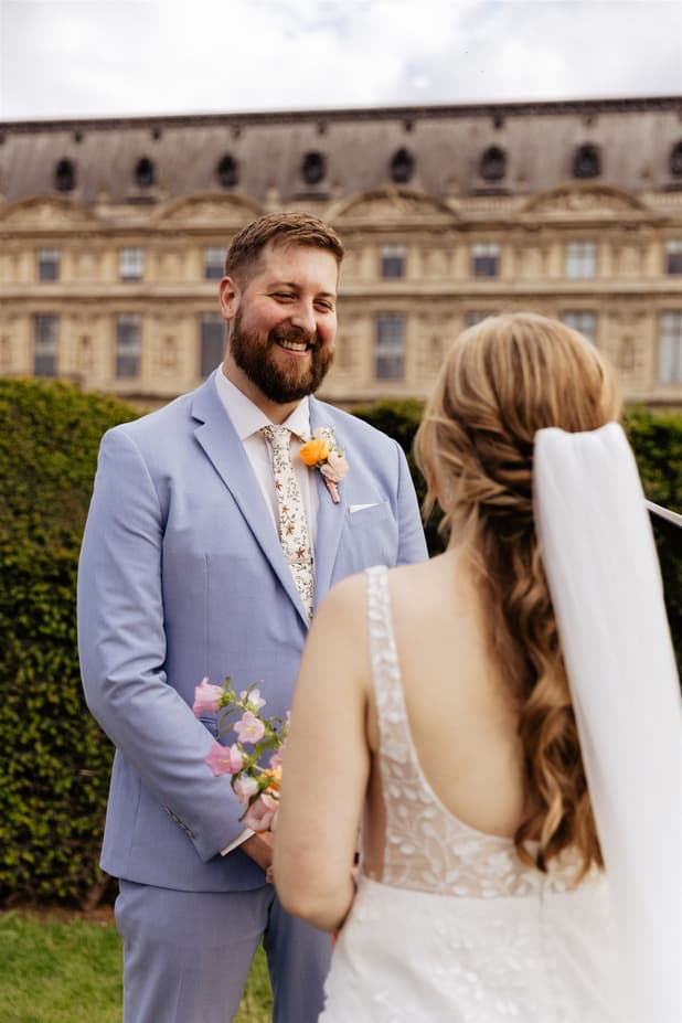 Bride and groom face each other in a Paris garden, with soft daylight and a historic stone façade behind them