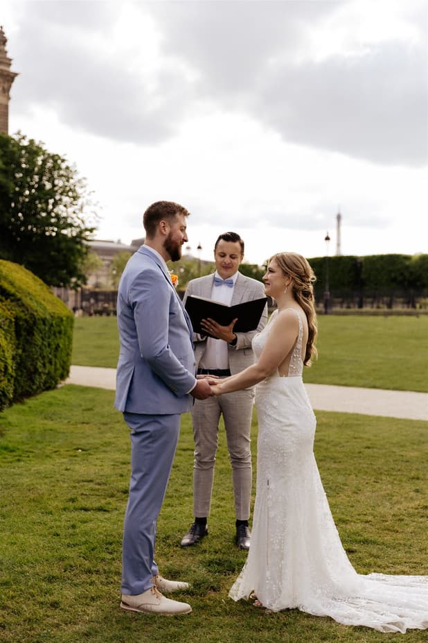 A&M holding hands before their officiant in the garden of the Louvre