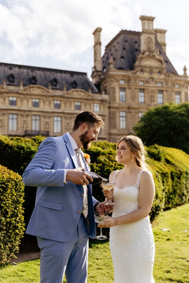 Bride and groom toast in a sunlit Paris garden before a grand palace facade