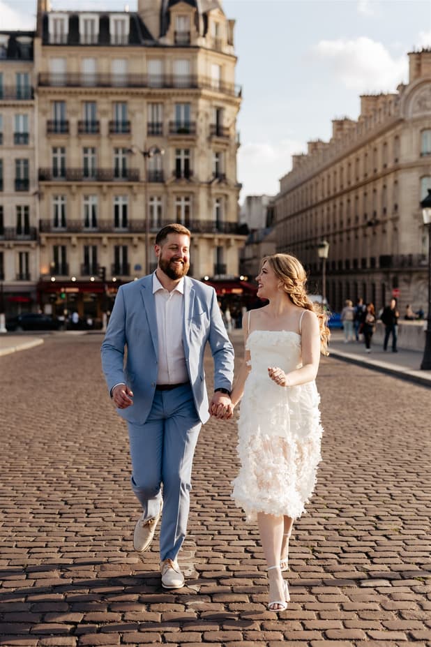 Bride and groom walk hand in hand on a cobblestone Paris street in warm evening light