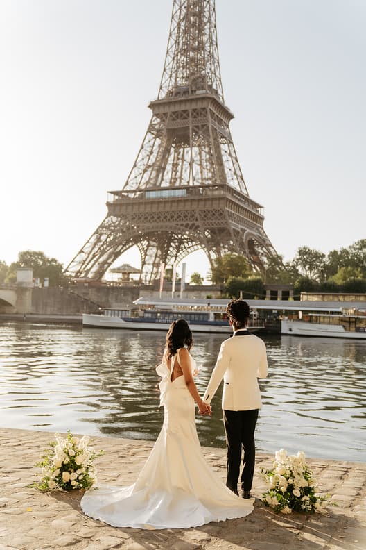 Bride and groom stand hand in hand by the Seine, with the Eiffel Tower glowing behind them