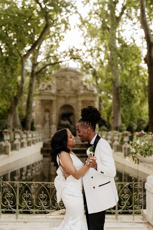 Bride and groom dance in a sunlit Paris garden by a reflecting pool and ornate stone fountain