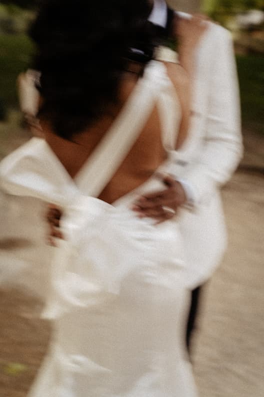 A bride and groom embrace on a Paris street, their white wedding clothes softly blurred